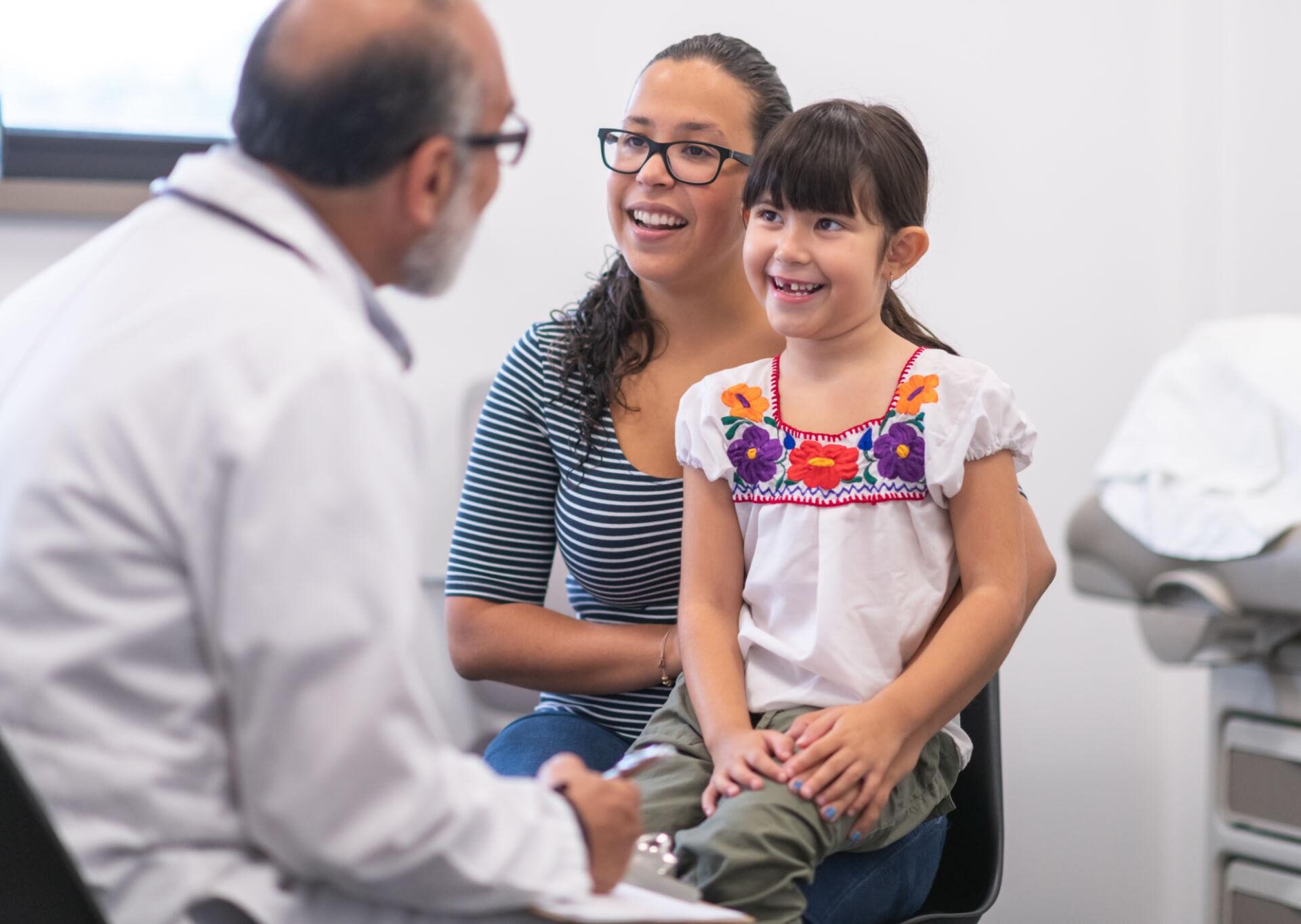 hispanic mother and young daughter with doctor in exam room